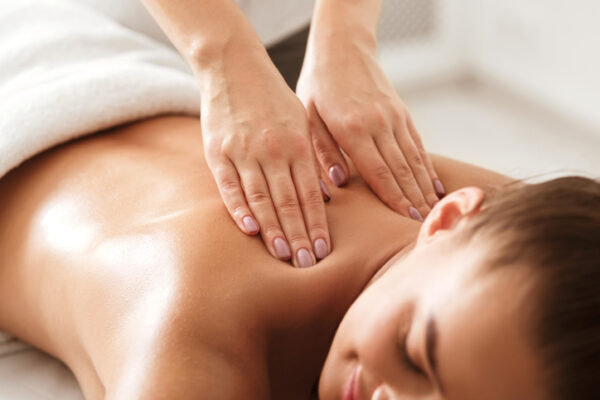 Young woman enjoying therapeutic neck massage in spa center, closeup